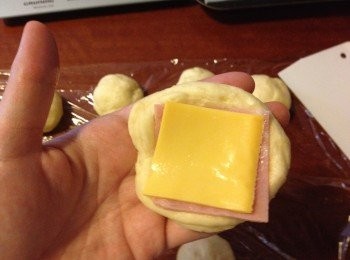 step6: 每個麵團輕輕壓平後放入一片火腿和芝士, 然後把四邊的麵團包入中間, 收口位放貼盤底