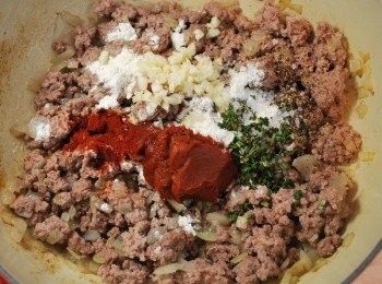 step6: 撒上麵粉，加入蕃茄糊、蒜末、迷迭香、紅椒粉、鹽及胡椒，翻炒均勻