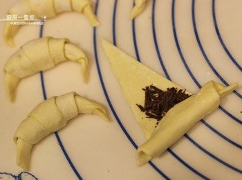 step7: 從三角形的底部向尖尖的頂部捲起，尖角處朝下，整成彎曲的可頌形狀。