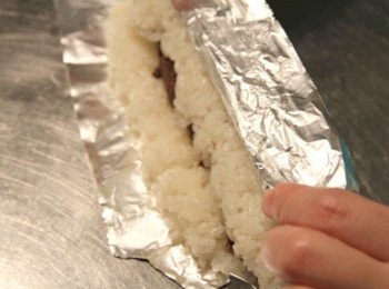 step2: 在錫箔紙在再鋪上一層保鮮膜，將煮好的美國圓糯米平鋪在保鮮膜上。中間再放入適量的紅豆沙後捲成壽司狀的米糕。再將米糕捲放入冰箱約10~20分鐘