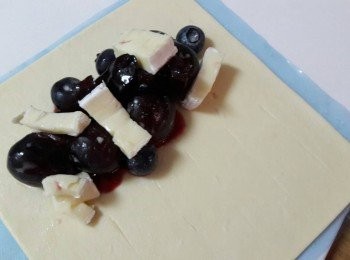 step6: 酥皮拿出把櫻桃 , 藍莓 , 果醬 , 起司丁堆在酥皮的一邊 , 另一邊劃上幾刀 , 邊邊用打散的蛋液掃上 , 把另一邊對摺 , 壓緊 , 再用叉子壓邊邊