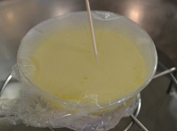 step6: 然後取一支牙籤，在保鮮膜上刺穿幾個小洞，讓蛋豆漿容易熟透，蓋上鍋蓋以小火繼續蒸6-8分鐘至熟透。（如果中間的蛋液還是水波狀的晃動，就表示還未蒸熟，要繼續蒸。也可用牙籤戳一下，沒有沾黏蛋夜，則表示熟透。）
