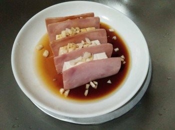 step2: 將豆腐【中華食品】、火腿【黑橋牌】放入蒸盤上，灑上蒜頭、放入少許的醬油【萬家香】，並在蒸盤上外鍋放2小杯水，轉大火清蒸7-10分鐘，