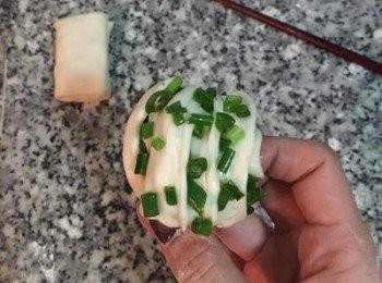 step19: 兩手抓著拉長的麵糰兩邊，一隻手略扭轉一下麵糰後繞過沒動的那隻手的食指，並將麵糰兩端的頭重疊後捏緊，便可擺放在蒸紙上，排入蒸籠中，