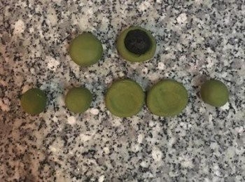 step10: 綠色麵糰等分成10份後揉圓，並用大姆指從中間壓出凹槽，放上冷凍過已變硬的芝麻內餡，用虎口慢慢均勻的包起來，將口收起捏緊，朝下放置，並用手指輕壓的方式把表面略微壓平。（芝麻內餡越圓則包餡和整圓都會更容易喔～）包好餡料的湯圓放回冷凍庫冰著。
