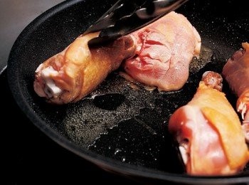 step7: 讓腿排肉最飽滿的部位抵著平底鍋的圓曲線，邊煎邊用油炸夾抬高肉塊，讓底下布滿油。棒腿肉煎出金黃色澤後，用油炸夾翻面，讓整體上色。