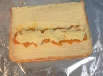 step18: 將鋁箔紙轉成橫的，留下一片蛋糕，先均勻抹上內餡，接著於中間區域加強多放一點內餡；將芒果丁擺放在中線旁，靠要捲的那邊，在芒果丁上抹上少許的內餡，蓋在芒果上，
