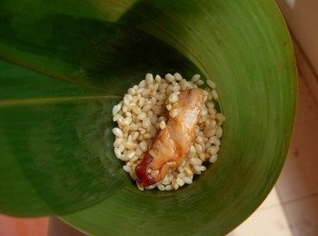 step3: 粽葉一前一後，相疊，拉起粽葉前端，圍一個半圈，翻過來裝<span class="group_1">食材</span>，底部二分之一糯米，然後加入花生，栗子豬肉，干貝等<span class="group_1">食材</span>，最上面再加一層糯米，填好<span class="group_1">食材</span>。