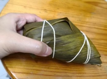 step3: 先用兩塊葉打交叉在中間摺後起一隻角，先放糯米，中央加豆沙饀再封上一層糯米蓋住將葉上下交叠摺向中央後，左右兩邊各加一片葉摺出四隻扁的底角用棉繩扎實