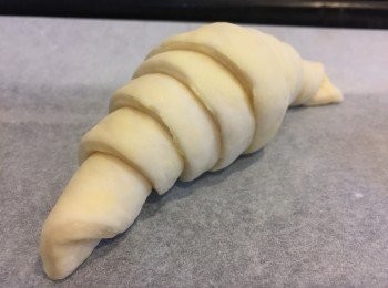 step11: 將三角形麵團輕力盡量拉長，由底部慢慢向上捲起，形成3.5-4.5層的標準牛角包造型，而且麵團收尾的角需要收向下，否則焗完出來會彈起。