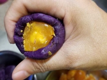 step7: 然後將紫薯用手掌搓至滑身,搓圓壓扁,中間加入一起磅的咸蛋黃包起搓圓成一粒粒,再包保鮮紙放入雪櫃待用