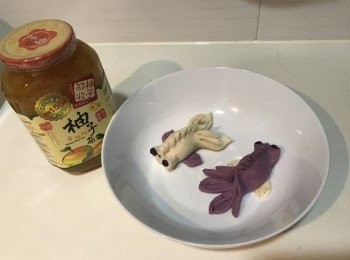 step3: （5）取一塊餃子包皮，放上南瓜餡料，然後把 上下中心點對摺後捏緊，一端捏緊邊緣至中心點稍過去一點。另一端的麵皮上，取對摺的兩個點向着捏好的部分推近，形成三個花瓣的形狀

（6（用刀切出金魚的尾巴，切4片尾巴，用勺子壓出金魚的紋路

（7）在捏緊，形成三個小圓圈，然後在眼睛的部位塞上兩小紫薯蓉，最後整理出金魚嘴即可