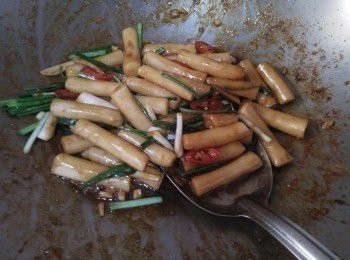 step2: 熱鍋後，放入1/8小匙芝麻油【福壽】，接著放入薑和蒜頭爆香， 約略1分鐘，等薑香氣出來，開中小火，依序放入年糕【澎湖年糕】、辣椒、青蔥、加入1/8小匙米酒、1/8小匙醬油、1/8小匙糖，並炒勻，約略3-5分鐘，