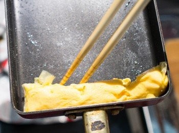 step12: 用筷子將蛋從煎鍋頂部（離自己遠的那一側）開始往回卷。
＊用筷子不熟練的可以用平面的鍋鏟或木斜鏟來卷。
捲至底部的蛋捲，往回推至前面。
＊有一點醜醜的沒關係喔！