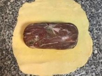 step11: 工作檯鋪上保鮮膜，放上橄好的派皮，將定型後的牛排去除保鮮膜，置於派皮中間，在牛排週圍塗上全蛋液；同樣的利用派皮下的保鮮膜將派皮完整包覆住牛排，兩邊則像包禮物ㄧ樣摺起，可切除其中一面多餘的派皮以免兩邊過厚。