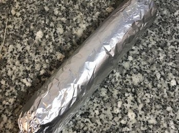 step17: 接著利用鋁箔紙將蛋糕捲，邊對邊捲起來，要記得蛋糕捲的接口處位置喔！因為放置時，需將接口處需朝下放。再來就是將兩邊旋緊即可，將蛋糕捲的接口處朝下擺放，並讓蛋糕捲抵著牆壁或物體，讓蛋糕捲不會滾動，這樣靜置15分鐘即可。