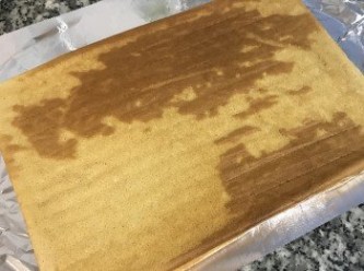 step15: 蛋糕降溫後，在桌上鋪一張鋁箔紙亮面朝上；將蛋糕倒放在鋁箔紙上，撕去烘焙紙；並在上面橫向劃刀方便捲起。
