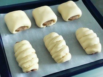 step5: 鬆弛完，逐份<span class="group_1">麵團</span>月擀薄成長方形後，包上午餐肉，<span class="group_1">麵團</span>兩邊短邊長度要比午餐肉短2cm左右， 不然<span class="group_1">麵團</span>焗完之後，會澎漲至完全包覆住午餐肉，看不到午餐肉外露的賣相。最後揑好收口向下，放在已鋪牛油紙的焗盤上。