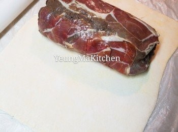 step10: 將已定型的牛柳拿出，拿走保鮮紙，抽出另一張保鮮紙，把即用酥皮放上，在酥皮各邊塗上蛋黃液。將鋪上酥皮的保鮮紙從底向上捲，將酥皮包住牛柳。包好後，將左右兩邊多餘的酥皮切掉，摺口封好後向下置放。用保鮮紙包好，再將左右兩端的保鮮紙扭緊。包好之後再放入雪櫃雪15分鐘定型。