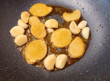 step3: 另開一個鍋放入黑麻油，用中小火慢慢煸香薑片，至薑片有一點金黃狀態，就加入蒜粒。