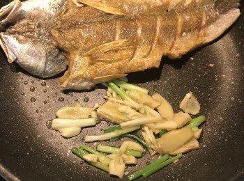 step8: 將魚推到鍋邊，利用餘油將蔥白、薑片和蒜片炒香；