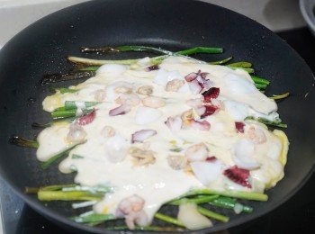 step4: 開中火加熱煎鍋，加入1湯匙油，油滾後將韮菜及蔥全部沾上麵糊，放入煎鍋煎約2分鐘至香脆，再加入海鮮、剩餘麵糊及蛋汁，煎2分鐘至香脆，再反面煎香。
📝令煎餅香脆的秘訣: * i)汆水讓海鮮不出水 * ii)用冰水開麵糊 * iii)韮菜葱要瀝乾撲粉 * iv) 油滾才下韮菜。 
📝雞蛋不與麵糊混合，分開煎的話蛋香會比較濃