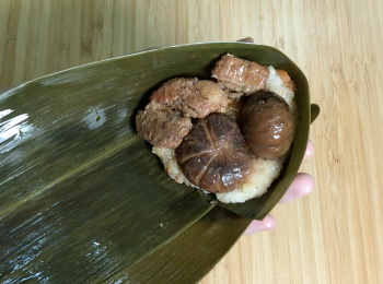 step7: 2塊粽葉，葉面向自己疊在一起，尾部（沒硬梗）摺漏斗型，放入糯米飯、鹹蛋黃、香菇、豬肉和栗子，用力壓緊，粽葉往上摺，兩邊往上摺，剩下粽葉往後摺