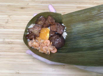 step6: 2塊粽葉，葉面向自己疊在一起，尾部（沒硬梗）摺漏斗型，放入花椰菜飯、鹹蛋黃、香菇、豬肉和蝦米，用力壓緊，粽葉往上摺，兩邊往上摺，剩下粽葉往後摺