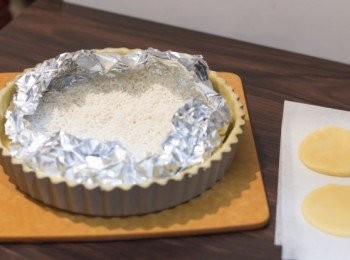 step12: <span class="group_1">撻皮</span>鋪好<span class="group_1">撻皮</span>之後放入冰箱（refrigerator）備用，同時預熱烤箱到攝氏180度。焗前用叉子於撻底平均插數下成平均分佈既小氣孔，<span class="group_1">撻皮</span>上鋪上烘焙紙再放上重石
（我不知把我的重石放到哪兒去了，手邊又沒有豆，所以隨手用了米來代替重石）
（烘焙紙用完了所以用上掃了一點油的錫紙，其實用烘焙紙會好一點）