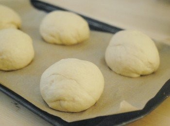 step5: 用手按壓麵團，排出空氣，分成6至8份。搓圓，放在鋪有烘焙紙的烤盤上，再用保鮮紙蓋好，靜置30分鐘，麵團會再脹大一點