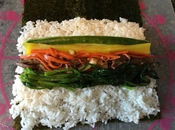 step3: 開始包喇！將紫菜粗的一面向上，鋪上白飯（約鋪滿2/3），順次序將牛肉/午餐肉，紅蘿蔔絲，黃蘿蔔條，青瓜條，菠菜（此時將根部切除），蛋條平均鋪在白飯中間位置。