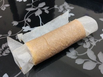 step8: 蛋糕冷卻後撕去牛油紙， 用同一牛油紙（因我做反   卷， 所以金黃面向上）輕力卷起蛋糕成卷狀， 待5分鐘 （這可令蛋糕加餡後較易卷起）