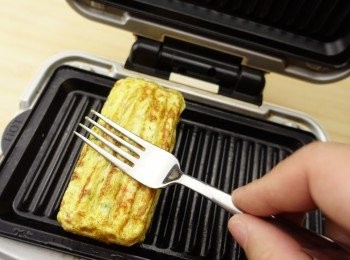 step4: 趁蛋漿未完全熟透，把蛋卷未端移向烤盤中間向下，用叉子按壓，煎至表面金黃。