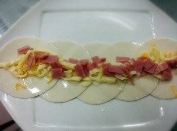 step2: 水餃皮排成一排把火腿和乳酪絲平鋪帶上面~四個面都要沾水~先折成一長條狀~再捲成一圈~要為壓一下好成形~