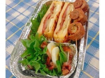 step9: 取鋁箔盒將對切的法式三明治放入，擺上蒜味吐司邊捲，另外用鋁箔紙做ㄧ個小盒，放入剩下的蛋片、生菜和洋蔥片，及切小塊的培根，並撒上少許黑胡椒粉即可。