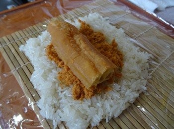 step3: 保鮮紙一片鋪在壽司蓆上，放上熱糯米飯，肉鬆和油條