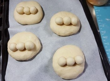 step9: 再將大麵糰按扁成餅形，將3粒細粒麵糰分別搽少許蛋白放於大麵糰上（位置放偏向下少許），輕輕按實接口位，再將做好形狀的麵糰包保鮮紙待最後發酵30分鐘