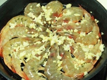 step2: 鐵鍋加入少許油，鍋面均勻鋪上薑片與蒜頭。3.將蝦圍著鍋內擺成一圈，均勻灑上黑胡椒粒與白胡椒粉，中火煎出蝦殼的香氣後，再均勻地淋上歩驟1.醃蝦的蒜末酒汁