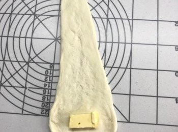 step4: 輕輕蓋上保鮮紙，鬆弛15分鐘, 
將麵團擀成上窄下闊的長形, 
放5g凍牛油在闊位，由闊向窄卷上，收口向下