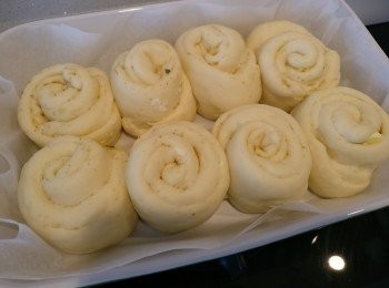 step5: 兩個鐘之後麵團增大約1倍，將它倒喺灑左麵粉嘅工作枱，再搓幾下揉成長條型，平均分做8份。

將分好嘅小麵團用麵粉棍/任何圓柱形嘅器皿碌平，大約係橢圓形咁上下。灑啲蒜粉，cheddar cheese同埋cream cheese喺麵團上，對摺，禁一禁邊沿等它唔漏餡。

將摺成長條型嘅麵團卷起，平排喺焗盤上放置溫暖嘅地方再發酵30mins~1hr. 

(小麵團之間要留2cm空間)