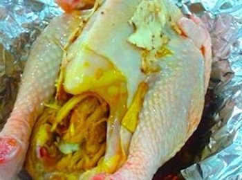 step2: 把鸡只摆放在锡纸（Aluminium foil)里后，把舂烂的姜，往鸡肚里塞满再将切小片的当归撒入鸡只上，再把鸡精倒入加入调味料后将锡纸包好。