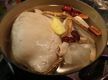 step8: 將汆燙好的肚包雞取出用清水洗一次。取另一湯鍋，加入適量水，放入餘下一半的藥材、白胡椒包、薑片和切下的雞爪，以大火煮滾後，轉中小火熬煮約1.5小時。（煲製期間要翻動一下肚包雞以免黏底，水不夠可加點熱水繼續熬煮。）