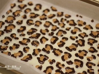 step11: 將裝有咖啡色麵糊的塑膠袋一角剪開一小孔，在烘焙紙上依模板畫出雙色豹紋圖案，請輕輕將烘焙紙底下的A4紙豹紋模板抽出，再送入160度C的烤箱中烘烤約1分鐘取出。