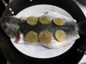 step2: 從頭到尾切開魚腹，沿著魚脊骨將魚片開，魚背朝上放在碟中，鹹檸檬切片碼放在魚身上。蒸鍋水開後，將蒸魚碟放入鍋中，大火蒸8分鐘左右。