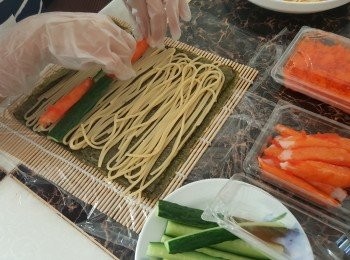 step6: 將壽司紫菜鋪在壽司竹卷上，囡囡代勞將都好的意粉平均鋪在紫菜上，擺入即食蟹柳、青瓜條，用壽司竹卷卷起定型