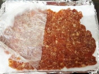 step6: 然後反轉，將烘焙紙放在錫紙上，再撕開上面的膠袋（用其他放法也可，將擀平的豬肉放在烘焙紙上）