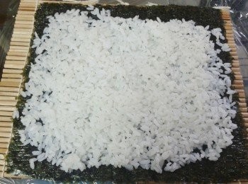 step3: 將一片紫菜放在壽司卷簾上，滑的一面向下。把飯平均鋪好，周邊留少許空間