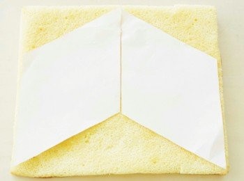 step12: 準備2張裁成菱形的紙片（兩條對角線長度分別為26cm與15cm），放在從紙烤模取出的海綿蛋糕上。依照紙型將蛋糕切成菱形。烘烤面朝上，用刷子沾上糖漿刷在2片海綿蛋糕上。