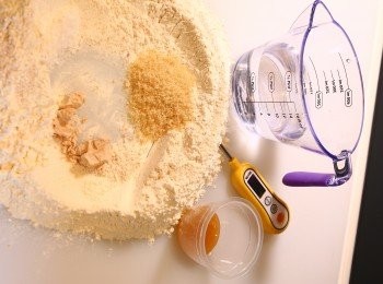 step2: 02\  所有材料量好；先放高筋麵粉和全麥麵粉，在麵粉堆中挖一個大圓圈，將酵母及黃糖放於麵粉圈內圓的一邊，將鹽放遠離酵母的另一邊； 加入蜜糖和水，用手拌混。