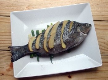 step4: 將魚先用鹽及米酒塗抹均勻,蒸魚盤也鋪上切段狀的蔥段,再將魚肉斜切幾道,每一道都要放入薑片,這樣可讓魚肉去腥提鮮。放蔥段在盤上的用意除了去腥提鮮之外,還可防止魚肉沾黏在盤上。